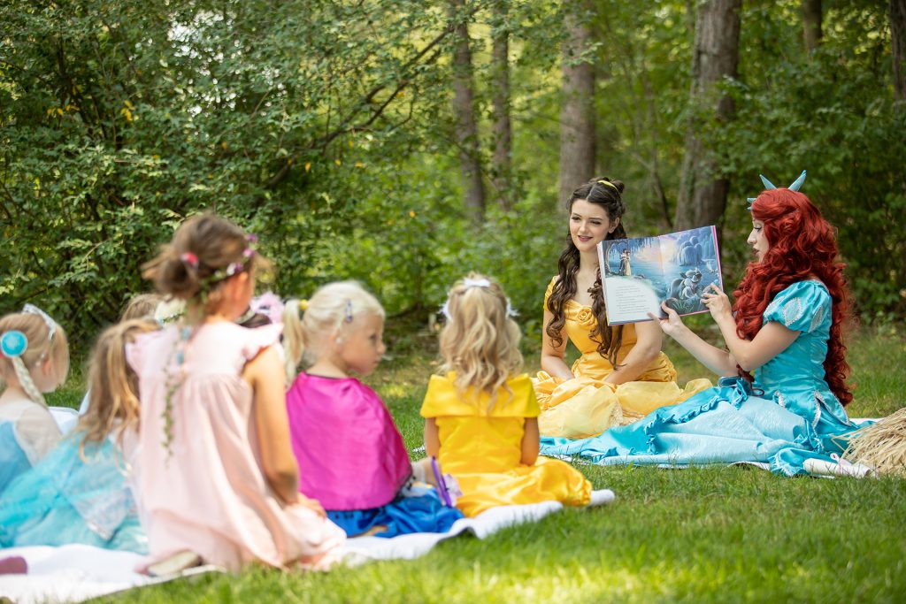 Princess Belle and the Little Mermaid reading to children at a princess party.