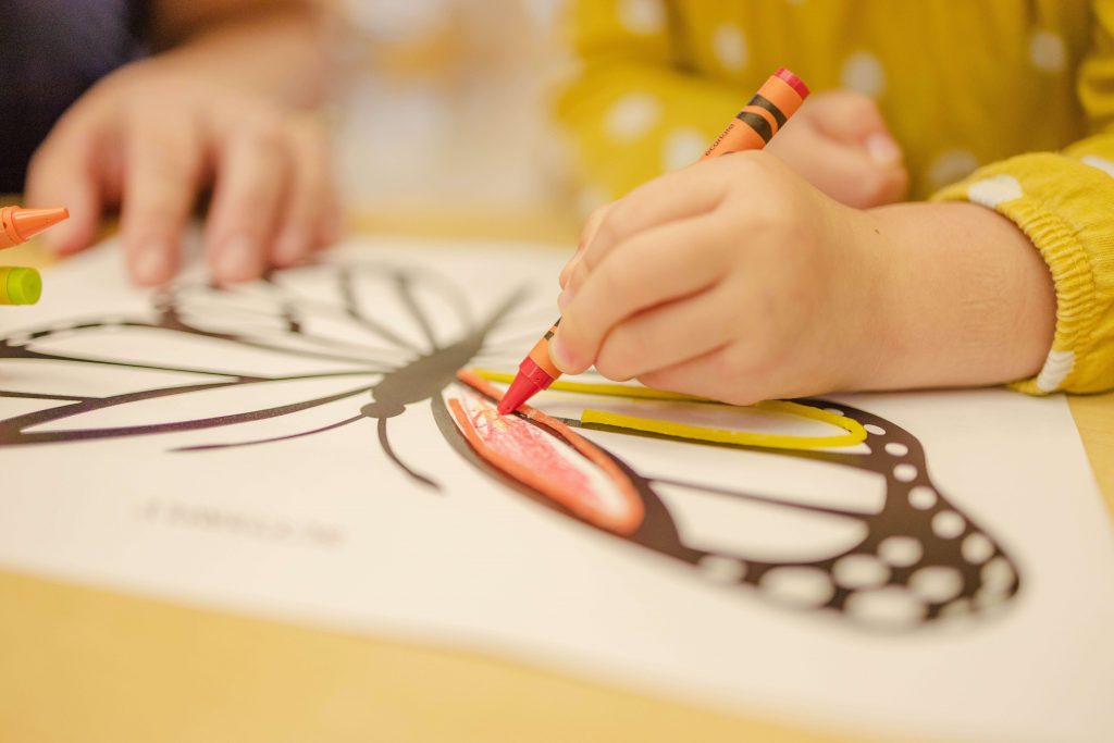 A young child colors in a picture of a butterfly with a crayon.