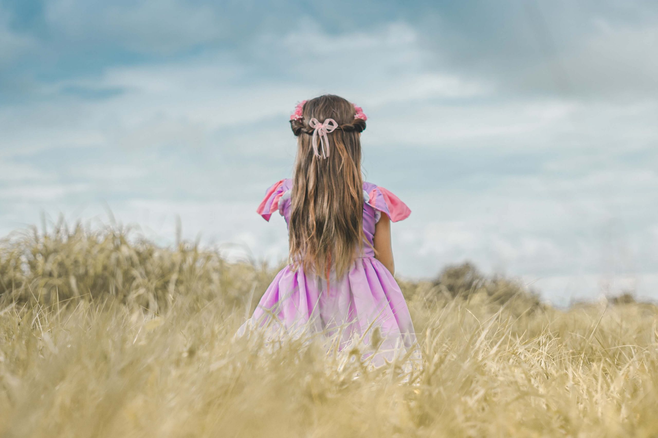 A young girl dressed as Rapunzel stands in a field