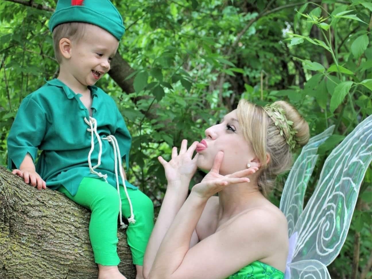 In this image, a woman playing Tinkerbell makes a funny face at a laughing little boy.