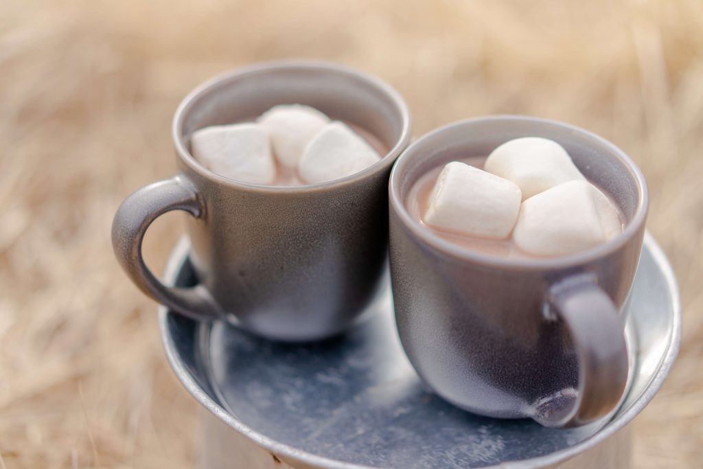 This picture features two cups of hot chocolate sitting next to one another. The cups contain marshmallows.