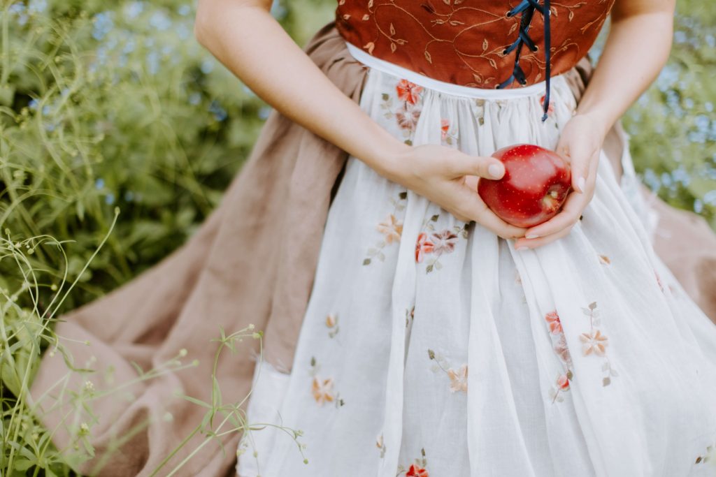 A woman in a simple linen dress sits while holding an apple.